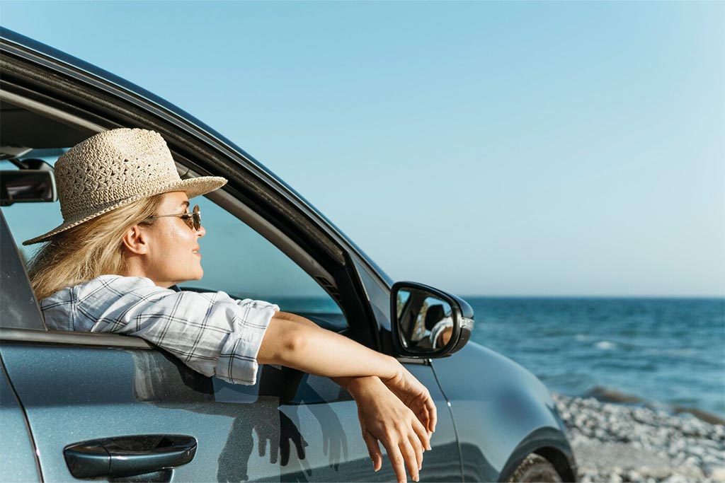 Lady in a car by the sea, sun shining on her face. Olives Seaside Villas, Plaka, Naxos